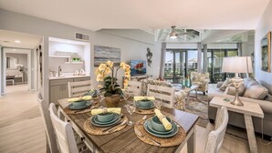 A dining area with a wooden table set for four, surrounded by chairs. There is a view of the living room and a balcony in the background. - **SUITE SANCTUARY** Oceanfront Condo & Pool + Last Key White Glove Service... (Key West)