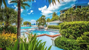 A pool area with multiple swimming pools, surrounded by lush greenery and palm trees. - **SUITE SANCTUARY** Oceanfront Condo & Pool + Last Key White Glove Service... (Key West)
