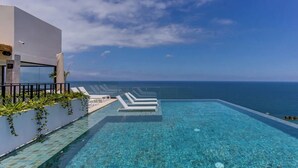 A modern infinity pool with clear blue water, white lounge chairs, and a view of the ocean. - Romantic Zone Penthouse w/Ocean Views (Puerto Vallarta)