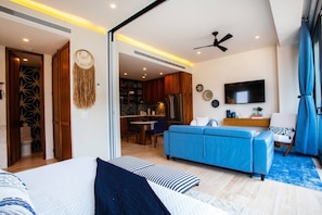 Ein modernes Hotelzimmer mit Bett, Sofa, Fernseher und einer Küchenzeile.