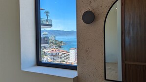 A bathroom with a large window, a round mirror, and a view of buildings and mountains. - Romantic Zone Penthouse w/Ocean Views (Puerto Vallarta)
