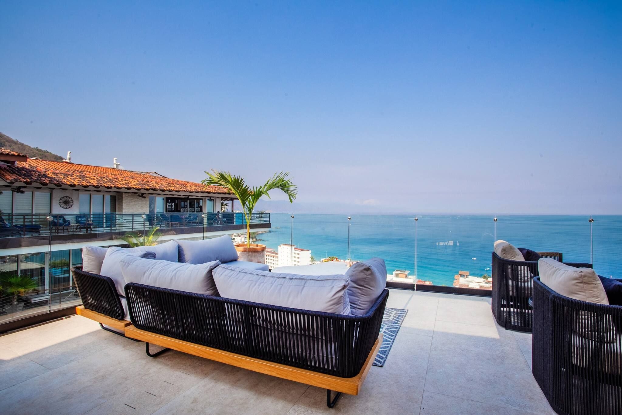A balcony with a sofa and chairs overlooking a clear blue sea.