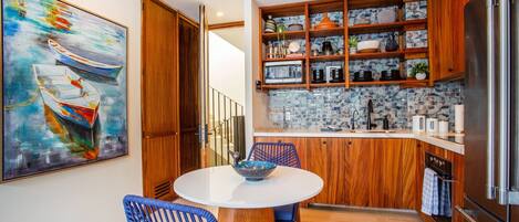 A modern kitchen with wooden cabinets, a stainless steel refrigerator, and a dining area with blue chairs.