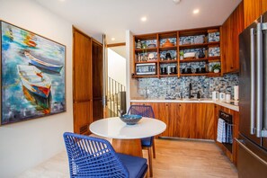 A modern kitchen with wooden cabinets, a stainless steel refrigerator, and a dining area with blue chairs.