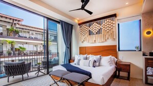 A modern bedroom with a large bed, a ceiling fan, a balcony with outdoor seating, and a view of a building. - Romantic Zone Penthouse w/Ocean Views (Puerto Vallarta)