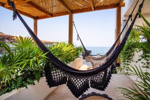 A hammock under a wooden pergola with a view of the sea.