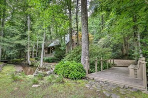 A cabin surrounded by a forest with a wooden deck and a small stream.