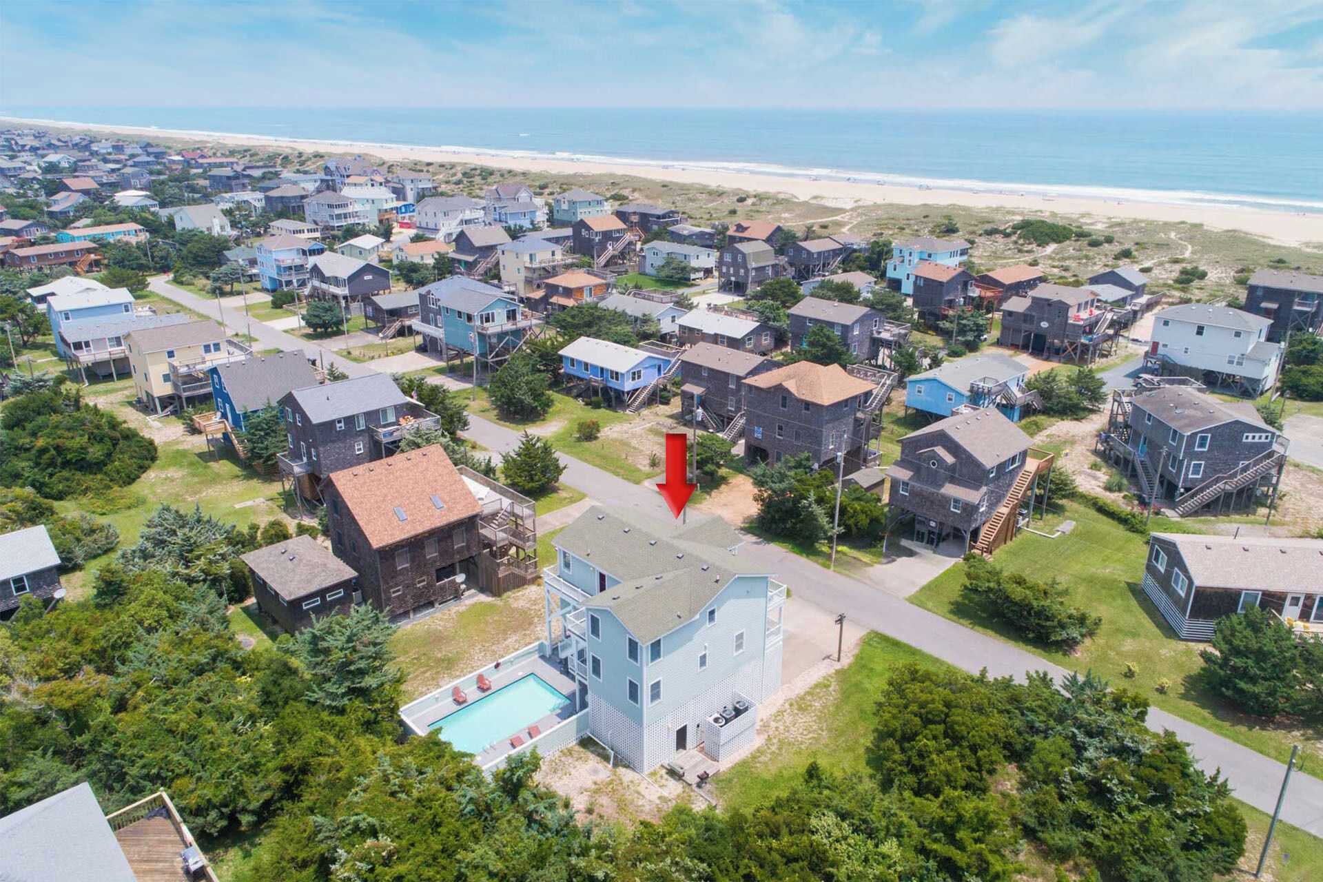 A coastal residential area with houses, a swimming pool, and a beach in the background.