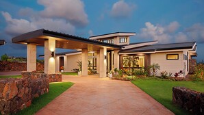 A modern house with a covered driveway, stone walls, and well-maintained landscaping. - Hale Mahina Hou: Luxe 4BR Home w/ Ocean Views, Infinity Pool & Outdoor Seating (Koloa)