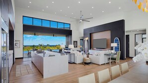 A spacious living area with a large TV, seating, and a view of the outdoors. - Hale Mahina Hou: Luxe 4BR Home w/ Ocean Views, Infinity Pool & Outdoor Seating (Koloa)