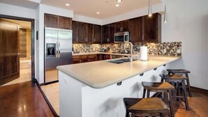 A modern kitchen with dark wooden cabinets, stainless steel appliances, a large island with stools, and a tiled backsplash. - Sprawling Condo | Central Downtown | Free Shuttle (Steamboat Springs)