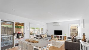 A spacious living area with a dining table, sofas, a TV, and a sliding glass door leading to a patio.