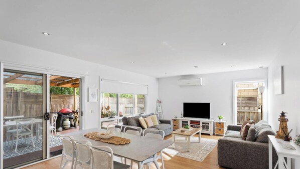 Un amplio salón con una mesa de comedor, sofás, televisor y un gran ventanal corredero que da a un patio.