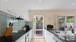 A modern kitchen with white cabinets, a glass countertop, a sink, and a microwave.