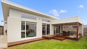 A modern two-story house with large sliding glass doors, a wooden deck, and a patio area. - Family Luxury 3 Bdr King Bed. (Newhaven)