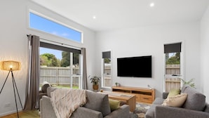 A modern living room with a large TV, grey sofas, a coffee table, and a floor lamp. - Family Luxury 3 Bdr King Bed. (Newhaven)
