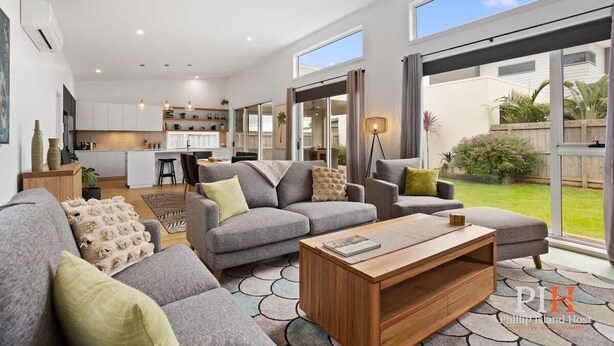 A spacious living area with a grey sofa set, a wooden coffee table, and a view of the kitchen and outdoor garden. - Family Luxury 3 Bdr King Bed. (Newhaven)