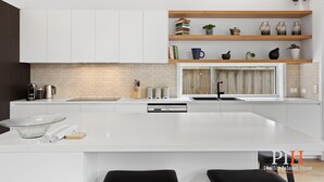 A modern kitchen with white cabinetry, a central island, and wooden shelves above. - Family Luxury 3 Bdr King Bed. (Newhaven)