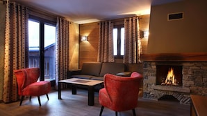 Ein gemütliches Wohnzimmer mit Kamin aus Stein, zwei roten Sesseln, einer Couch und einem Couchtisch.