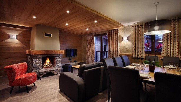 A cozy living room with a stone fireplace, leather sofas, a dining area with a table set for four, and a large window with curtains. - Wifi, fitness, swimming pool, sauna, hammam, balcony, tv, ski locker, 72m², Les Arcs (Les Arcs)