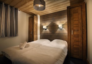 Un dormitorio con cabecera de madera, dos lámparas de pared y una cama grande con ropa de cama blanca.