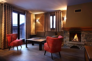 A cozy living room with a stone fireplace, two red armchairs, a sofa, and a coffee table.