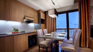 Una cocina moderna con armarios de madera, una zona de comedor con mesa de vidrio y vistas a un paisaje nevado a través de amplios ventanales.