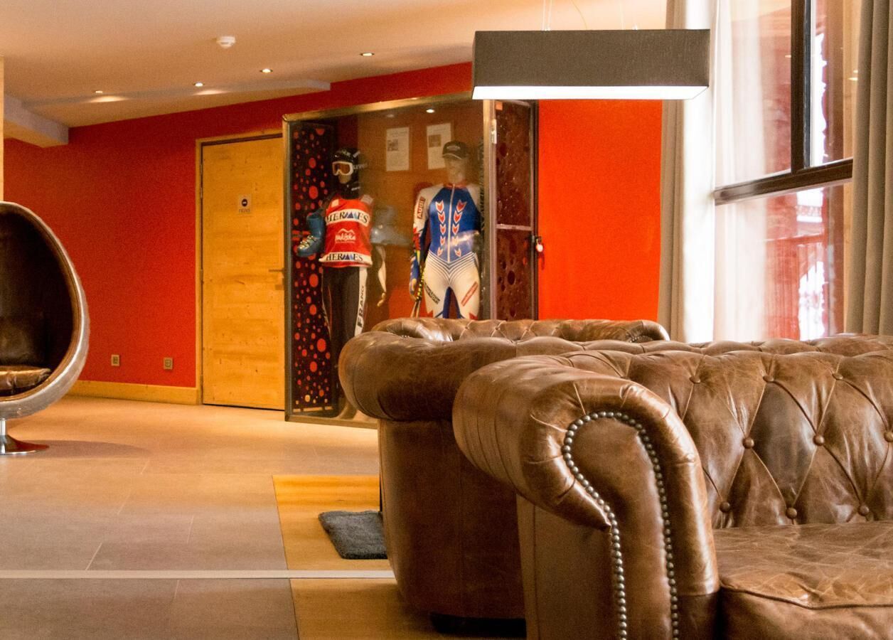 A lobby with a brown leather sofa, a red wall, and a mannequin in sports attire.