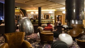 Un hall con sillones de cuero, una gran escultura metálica y una zona de bar con un barman.