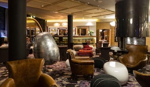 A lobby with leather armchairs, a large metallic sculpture, and a bar area with a bartender.