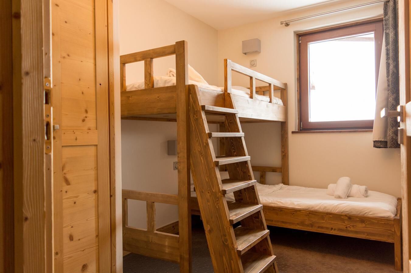 A bunk bed room with a wooden ladder, a window, and a door.