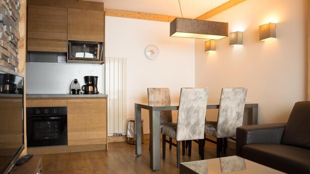 Eine moderne Küche mit Holzschränken, einem eingebauten Backofen und einer Mikrowelle. Es gibt eine Essecke mit Tisch und Stühlen sowie ein Sofa im Wohnzimmer.