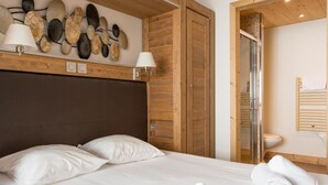 Un dormitorio con cama, dos lámparas de noche, cabecera de madera, obra de arte en la pared, armario de madera, zona de ducha y una toalla sobre la cama.