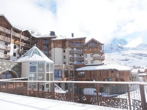 A ski resort with wooden buildings, a glass-roofed structure, and snow-covered mountains in the background.