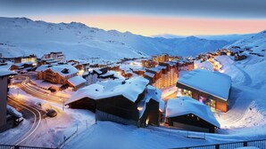 Un pueblo montañoso cubierto de nieve al anochecer, con edificios iluminados y carreteras serpenteantes.