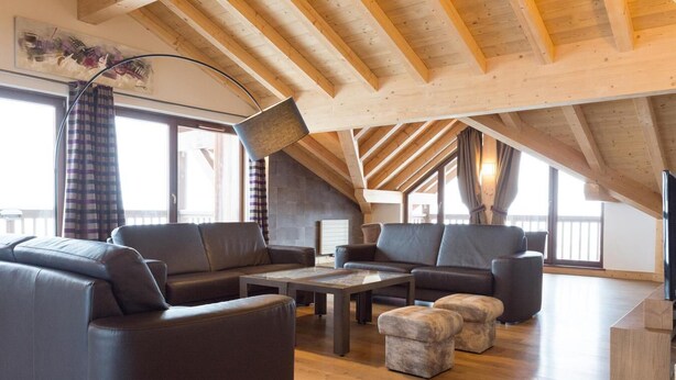 Amplio espacio tipo loft con techos altos y vigas de madera a la vista, con sofás de cuero, una mesa de centro y una chimenea.