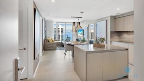 Una cocina moderna con una isla central, un comedor con mesa y sillas, y vistas de la ciudad a través de amplios ventanales.