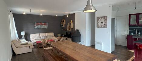 Amplia sala de estar con una gran mesa de comedor de madera, un sofá y una cocina con armarios rojos.