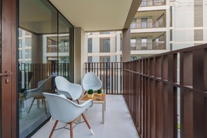 A balcony with two white chairs, a small table with potted plants, and a view of adjacent buildings.