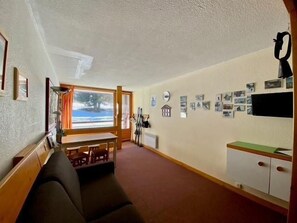 A cozy room with a sofa, a wooden table, a window, and a wall adorned with photos.