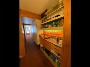 A narrow hallway leading to a kitchen with wooden cabinets and shelves.