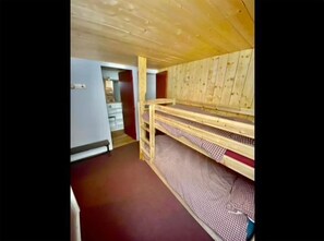 A room with a bunk bed, a wooden ceiling, and a red carpet.