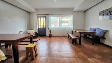 A spacious room with a high ceiling, a ceiling fan, a large window with curtains, a door, and a wall-mounted painting.