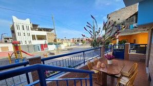 A balcony with a table and chairs, a view of the street, and a playground. - Txada Hostel (Praia)