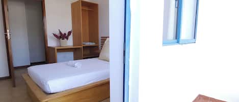 Ein Schlafzimmer mit einem Bett, einem Holzschrank, einer Zimmerpflanze und einem Fenster.