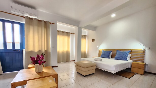 A hotel room with a bed, bedside table, and a small table with a vase of flowers. - Txada Hostel (Praia)