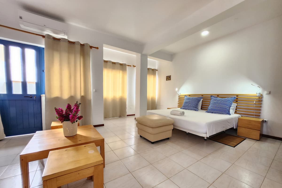A hotel room with a bed, bedside table, and a small table with a vase of flowers.