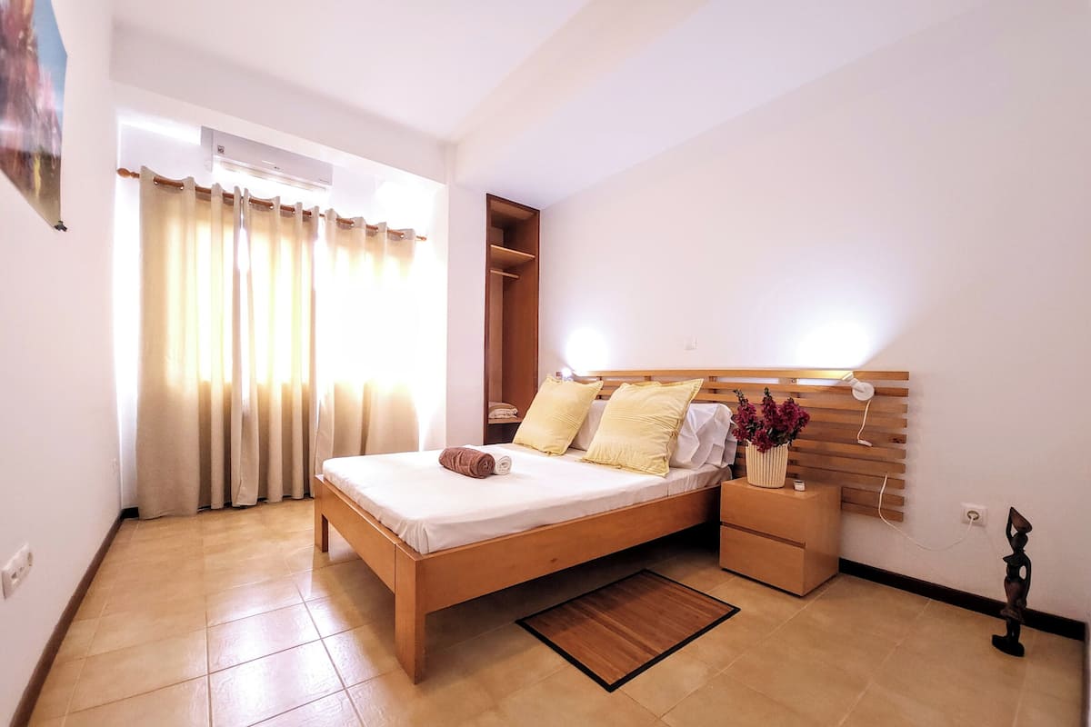 A neatly arranged bedroom with a wooden bed, a bedside table with a vase of flowers, a nightstand, and a built-in wardrobe.