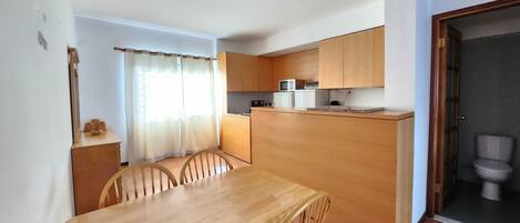 Una cocina compacta con armarios de madera, una mesa de comedor con sillas y una pequeña isla con microondas.