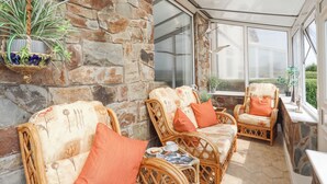 A sunroom with wicker furniture, stone walls, and a view through large windows. - Morlais (Ty Croes)
